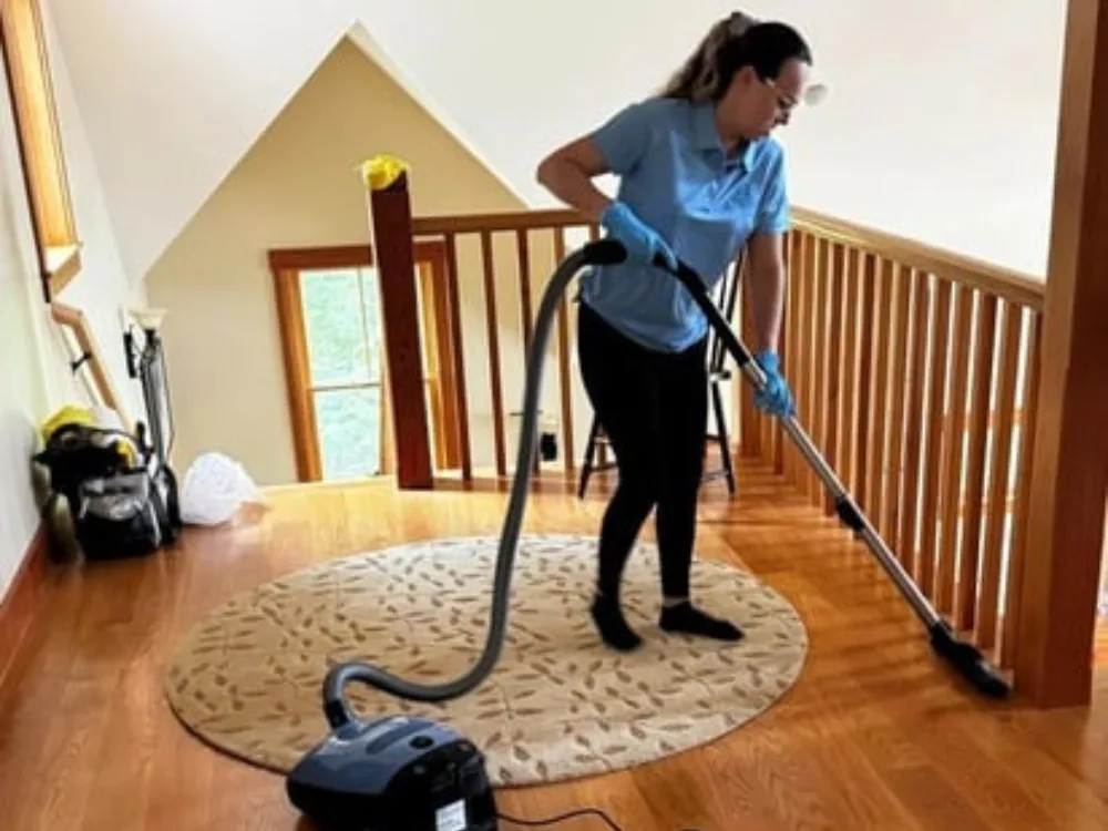 Worker conducting hardwood floor vacuuming around a round rug.