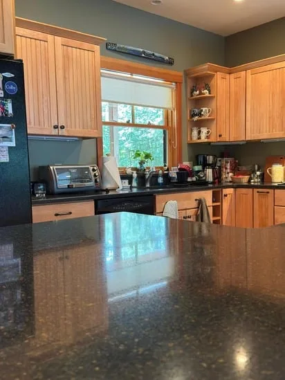 Close-up of a dark granite countertop reflecting a window after a professional deep kitchen cleaning service.