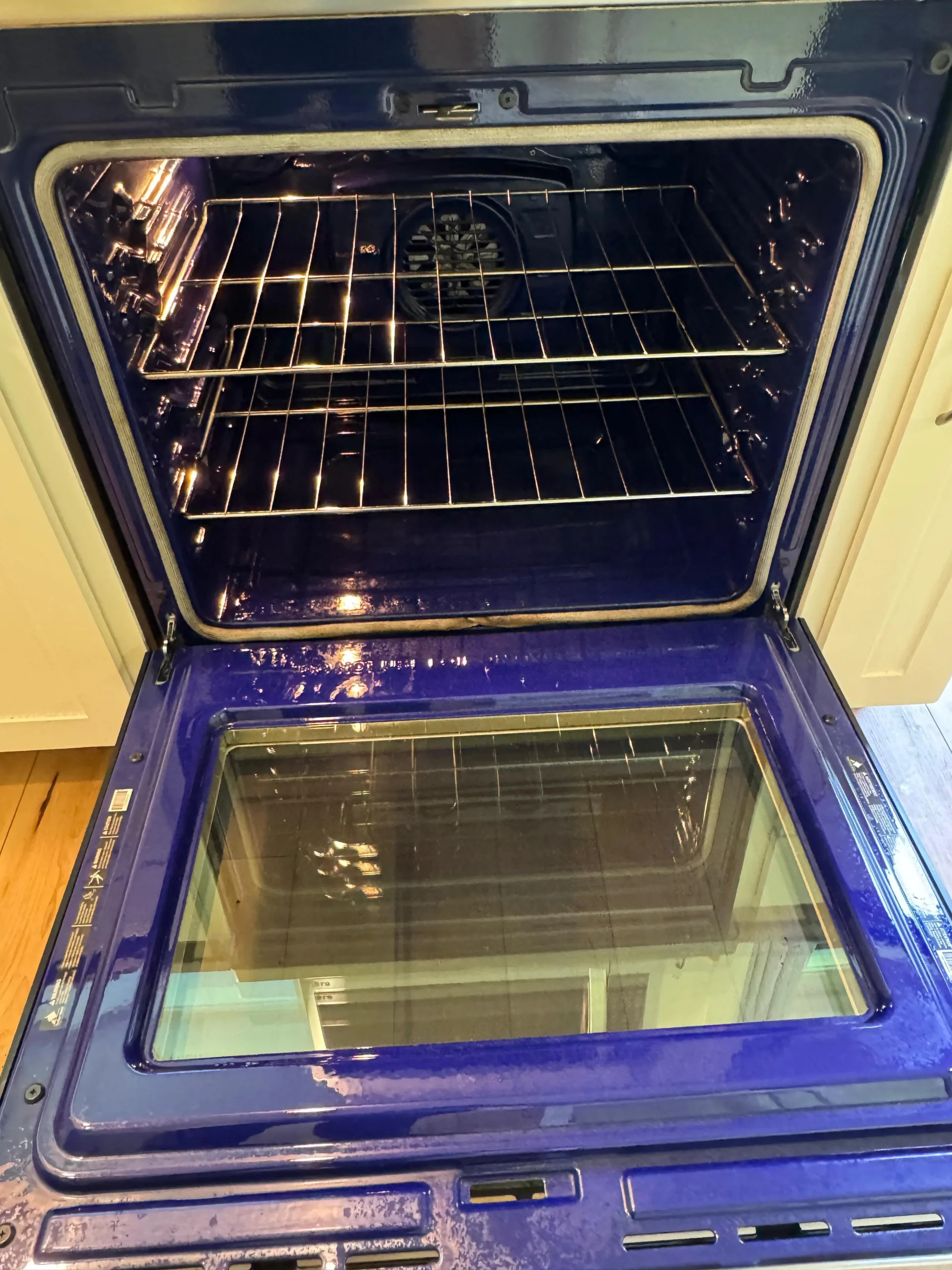 A professional deep oven cleaning result showing a spotless blue porcelain interior with polished chrome racks and a clear glass door.