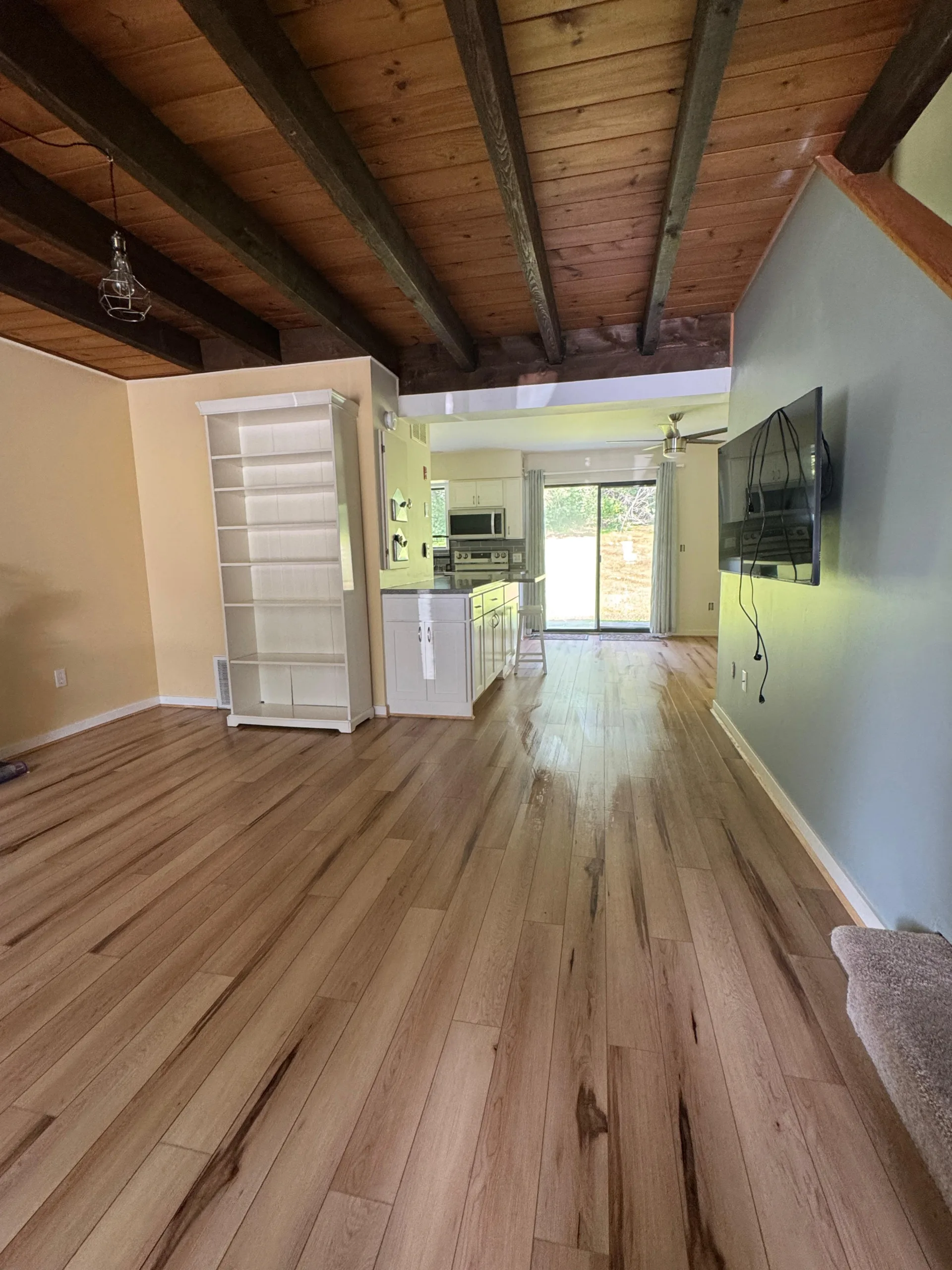 Move-in cleaning service results in a residential living room featuring polished floors, a clean kitchen, and vaulted timber ceilings.
